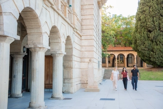 Three students walking together outside past the Winthrop Hall arches and Reflection Pond.